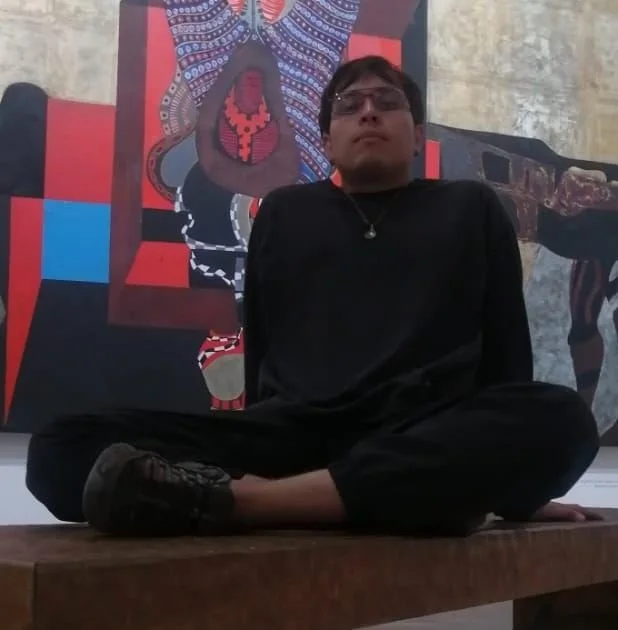 Josué Mazatzin sentado frente a una obra visual